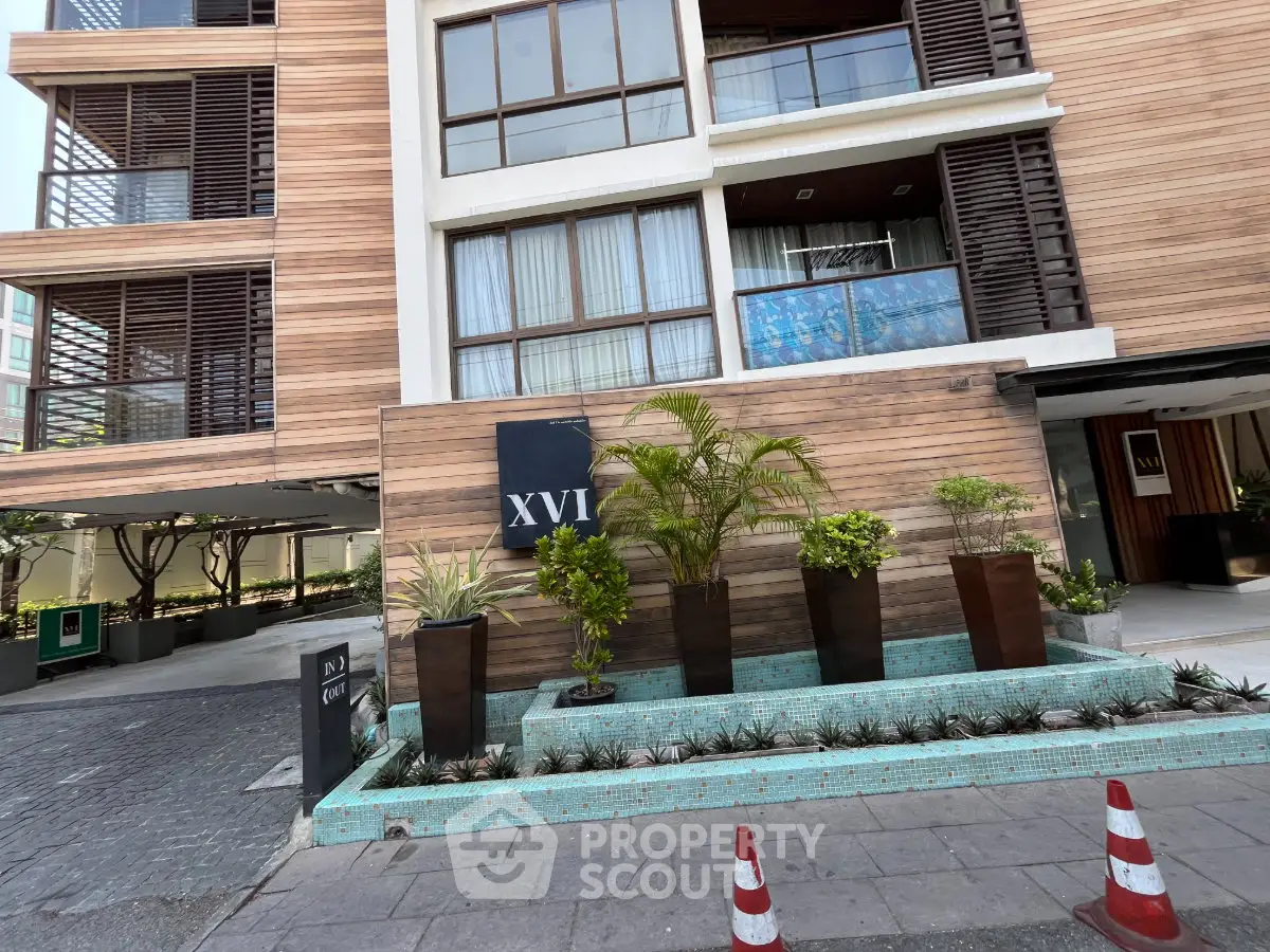 Modern building exterior with stylish wooden facade and lush landscaping at entrance.