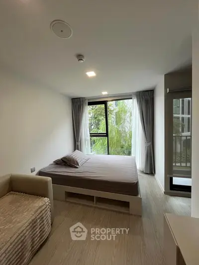 Modern bedroom with large window and cozy bed, offering serene garden views.