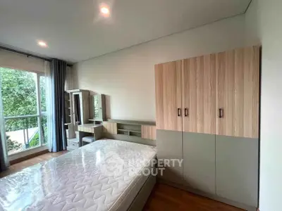 Modern bedroom with large window and stylish furniture, offering a serene view of lush greenery.