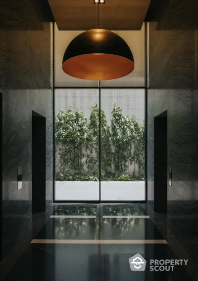 Elegant modern building entrance with stylish lighting and lush greenery view.