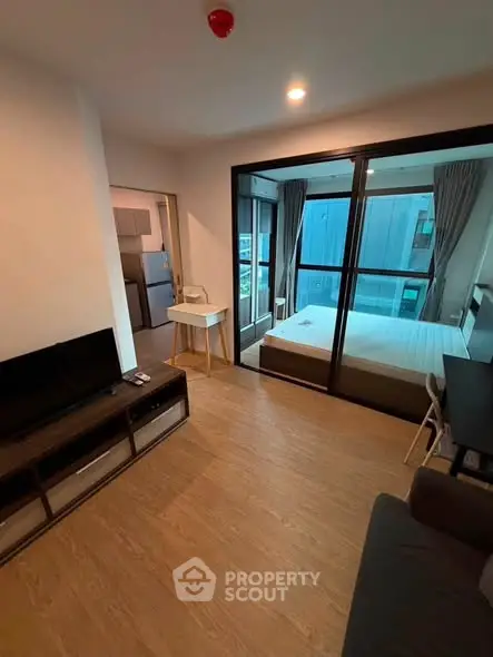 Modern apartment interior with open living room and bedroom, featuring sleek furniture and large windows.