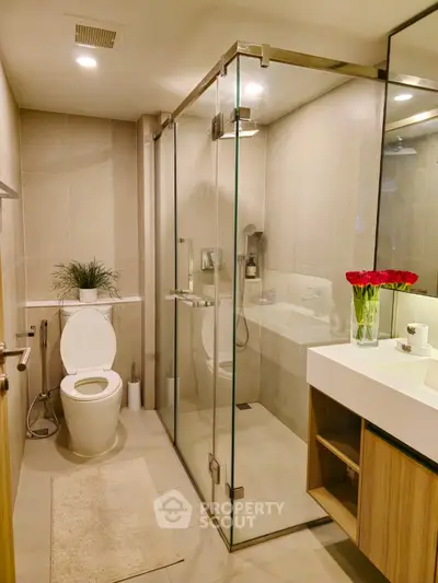 Modern bathroom with glass shower enclosure, sleek fixtures, and elegant vanity unit, accented by vibrant red flowers for a touch of color.