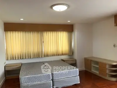 Spacious bedroom with twin beds and wooden furniture, featuring large window with curtains.