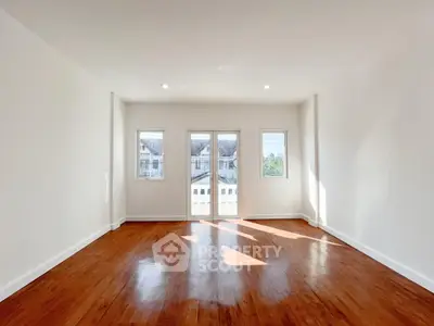 Spacious sunlit room with hardwood floors and large windows offering a serene view.
