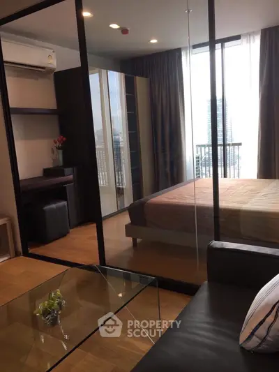 Modern bedroom with glass partition and city view, featuring sleek furniture and natural light.