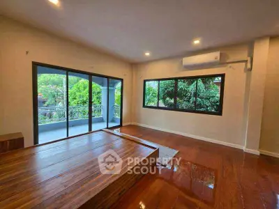 Spacious living room with wooden flooring and large windows overlooking greenery.