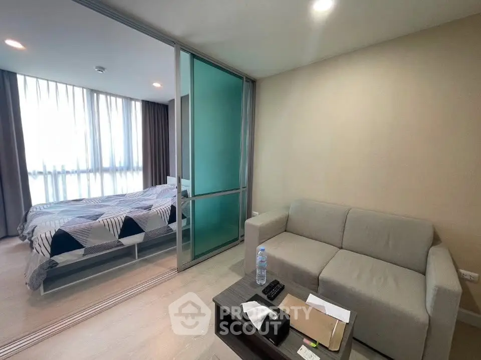 Modern apartment interior with cozy living room and bedroom separated by glass partition.