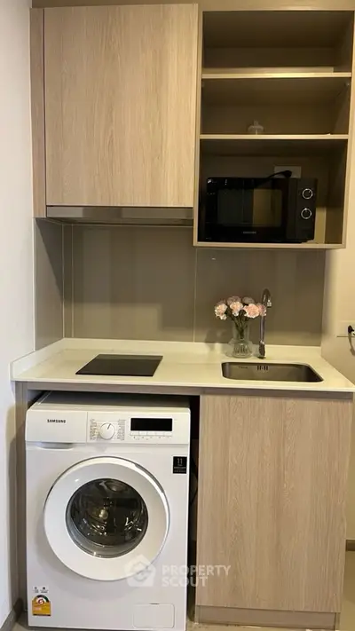 Compact modern kitchen with washing machine, microwave, and sleek cabinetry, perfect for urban living.