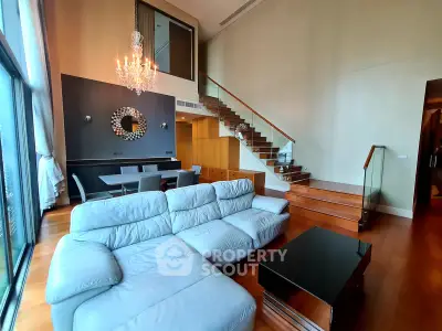 Luxurious living room with high ceiling, elegant chandelier, and modern staircase in a stylish apartment.