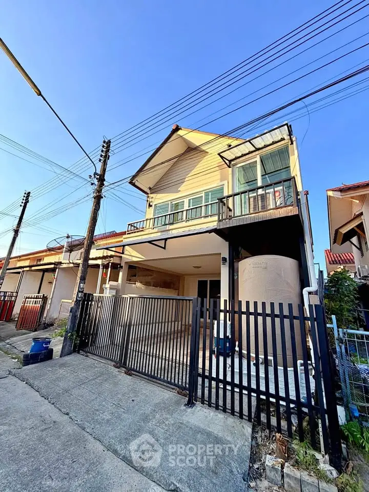 Charming two-story house with balcony and gated entrance in a suburban neighborhood.