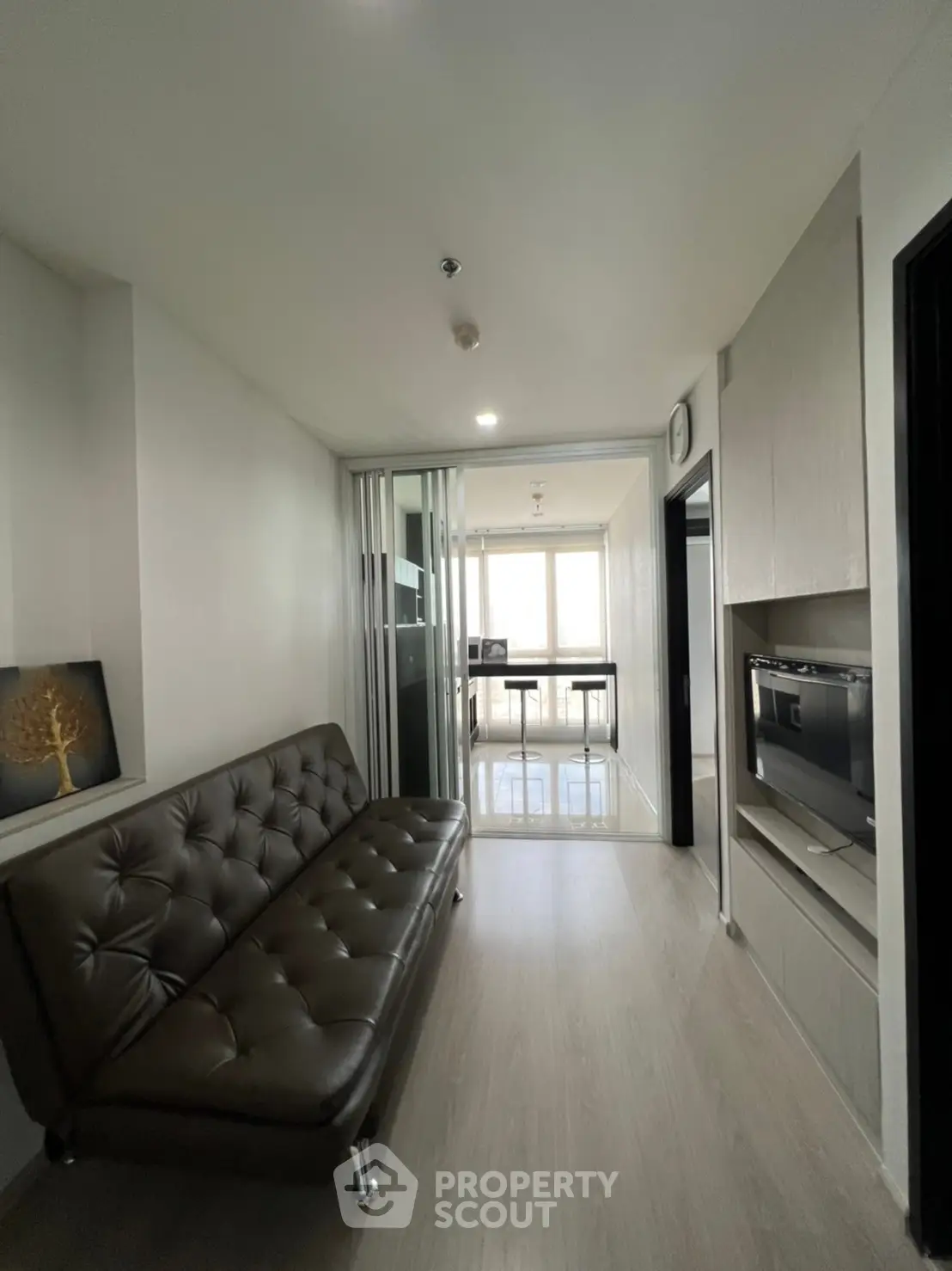 Modern apartment with sleek living room and glass partition leading to a bright study area.