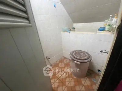 Compact bathroom with sloped ceiling and tiled floor, featuring essential toiletries and a waste bin.