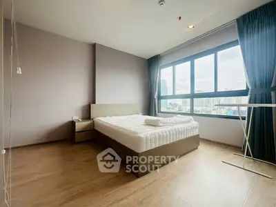 Spacious bedroom with large window offering city views, featuring modern furnishings and wooden flooring.