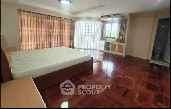 Spacious bedroom with wooden flooring and large windows for natural light