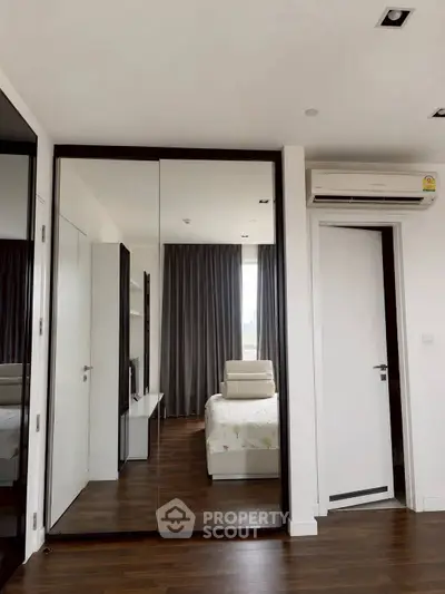 Modern bedroom with mirrored wardrobe and air conditioning, featuring sleek design and natural light.