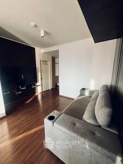 Modern living room with sleek design and comfortable gray sofa, featuring a wall-mounted TV and wooden flooring.