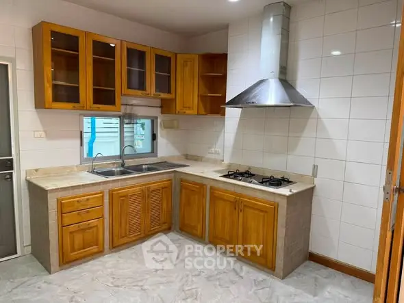 Spacious kitchen with wooden cabinets and modern gas stove in a bright, tiled setting.