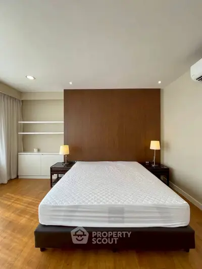 Spacious bedroom with modern design and natural light, featuring a comfortable bed and elegant wooden flooring.