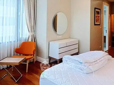 Modern bedroom with stylish furniture and natural light, featuring a cozy orange chair and elegant decor.