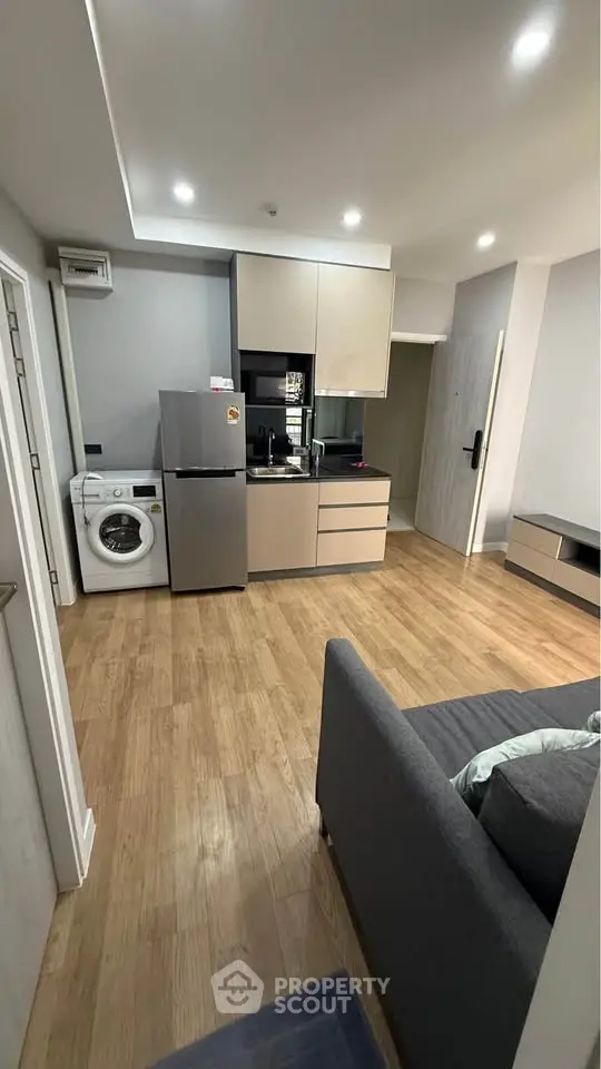 Modern apartment interior with kitchen and living area featuring wooden flooring and sleek appliances.