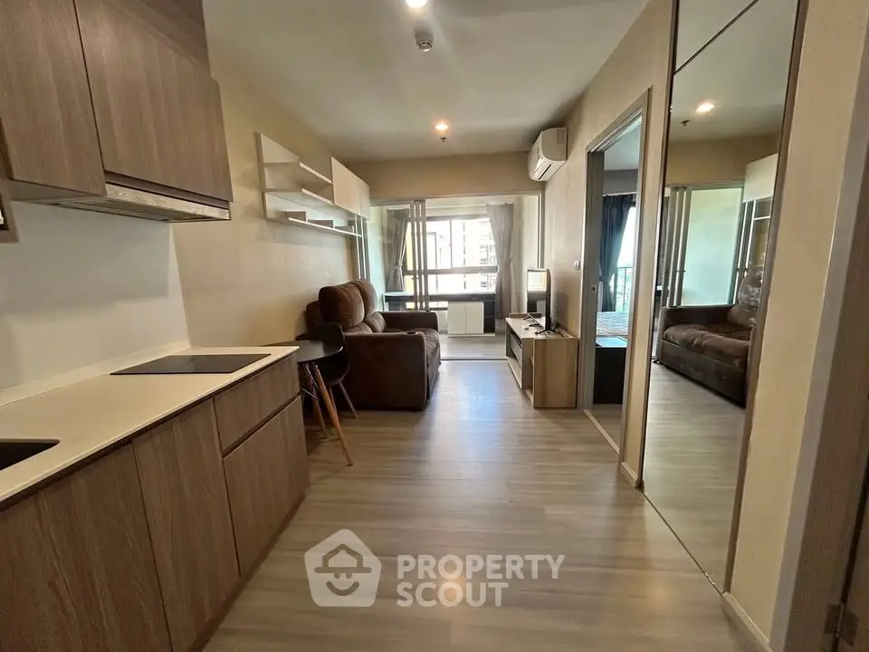 Modern open-layout living room with kitchen, featuring sleek wooden cabinetry and cozy seating area.
