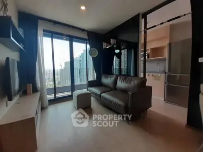 Modern living room with balcony and city view, featuring sleek furniture and open kitchen layout.