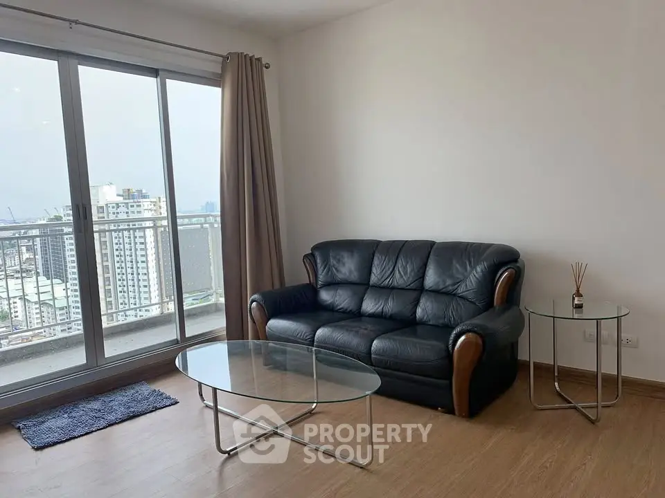 Modern living room with leather sofa and glass tables, featuring a stunning city view from the balcony.