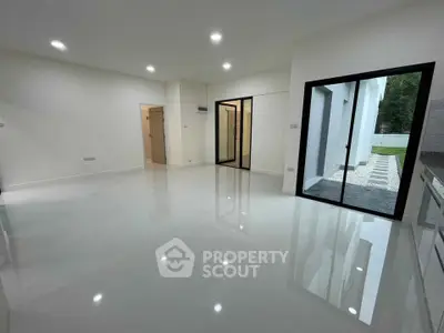Spacious modern living room with glossy floors and sliding glass doors opening to a serene garden view.