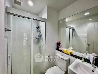 Modern bathroom with glass shower and large mirror in sleek apartment.