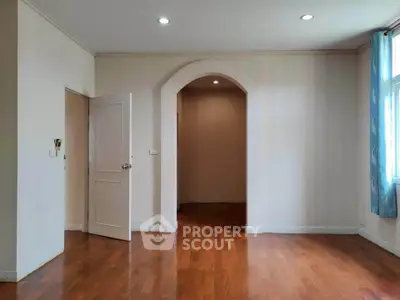 Spacious empty room with wooden flooring and archway, ideal for customization.