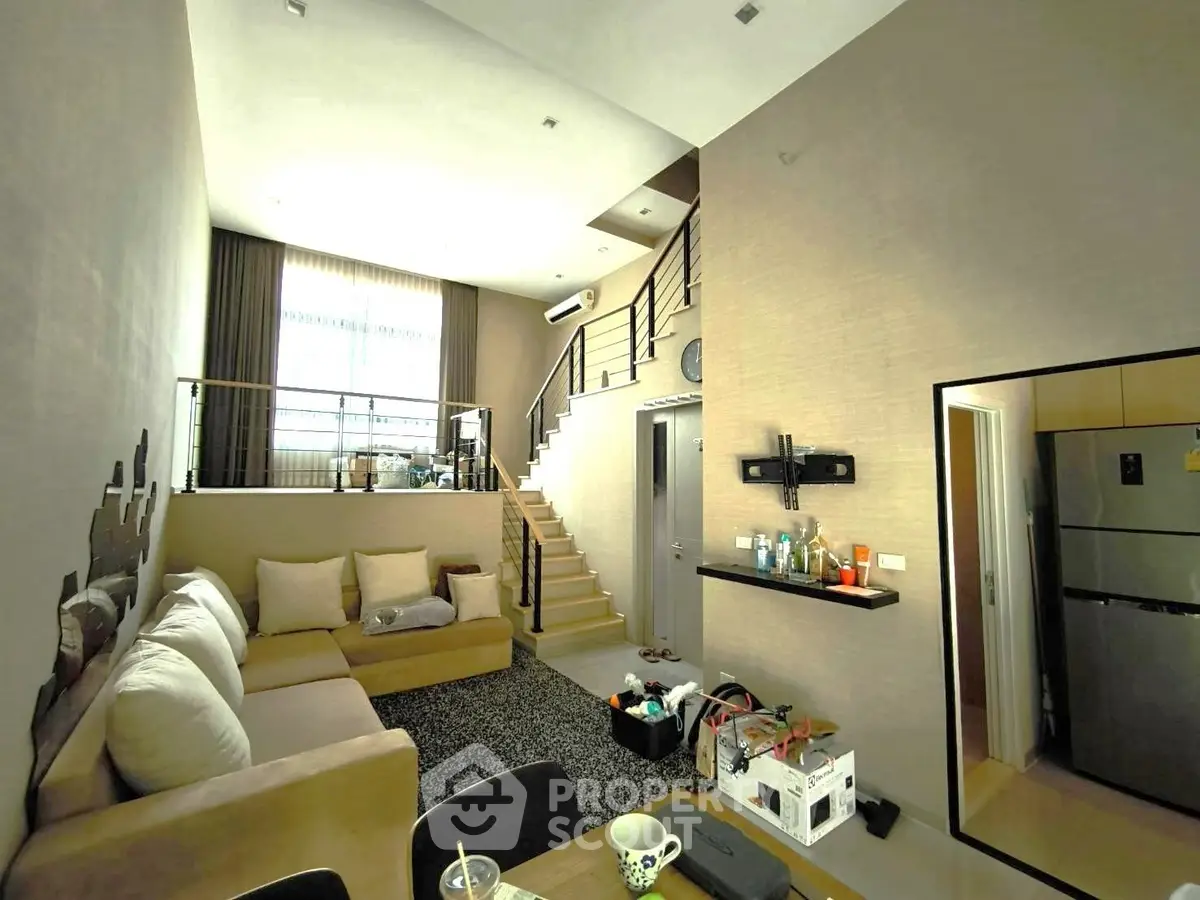 Modern loft-style living room with high ceilings and staircase, featuring cozy seating and contemporary decor.