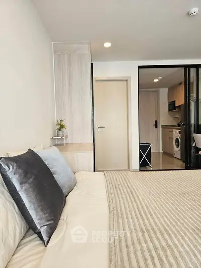 Modern bedroom with cozy bed and view into a stylish kitchen area