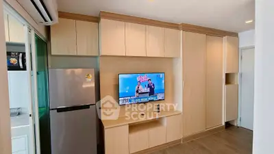 Modern living room with built-in wooden cabinets and mounted TV, adjacent to a sleek kitchen area.