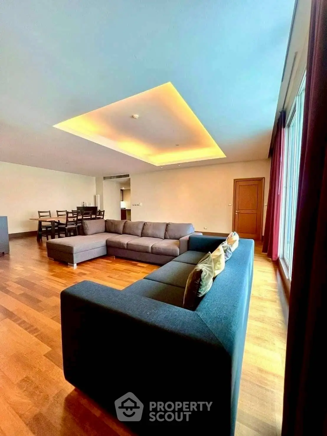 Spacious living room with modern sectional sofa and elegant dining area, featuring warm wooden flooring and ambient lighting.
