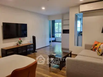 Modern living room with hardwood floors, stylish furniture, and large TV, leading to a bright bedroom.