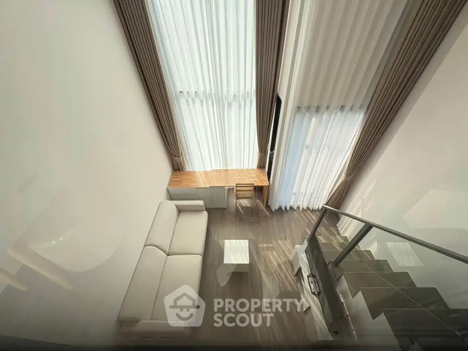 Modern loft-style living room with high ceilings and large windows, featuring a cozy sofa and stylish decor.