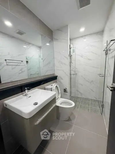 Modern bathroom with sleek fixtures and glass shower enclosure in contemporary apartment.