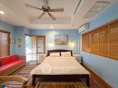 Spacious bedroom with modern decor, featuring a ceiling fan, air conditioning, and natural light from large windows.