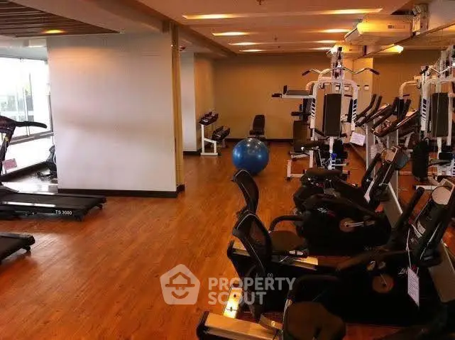 Spacious gym with modern fitness equipment and wooden flooring in a residential building.