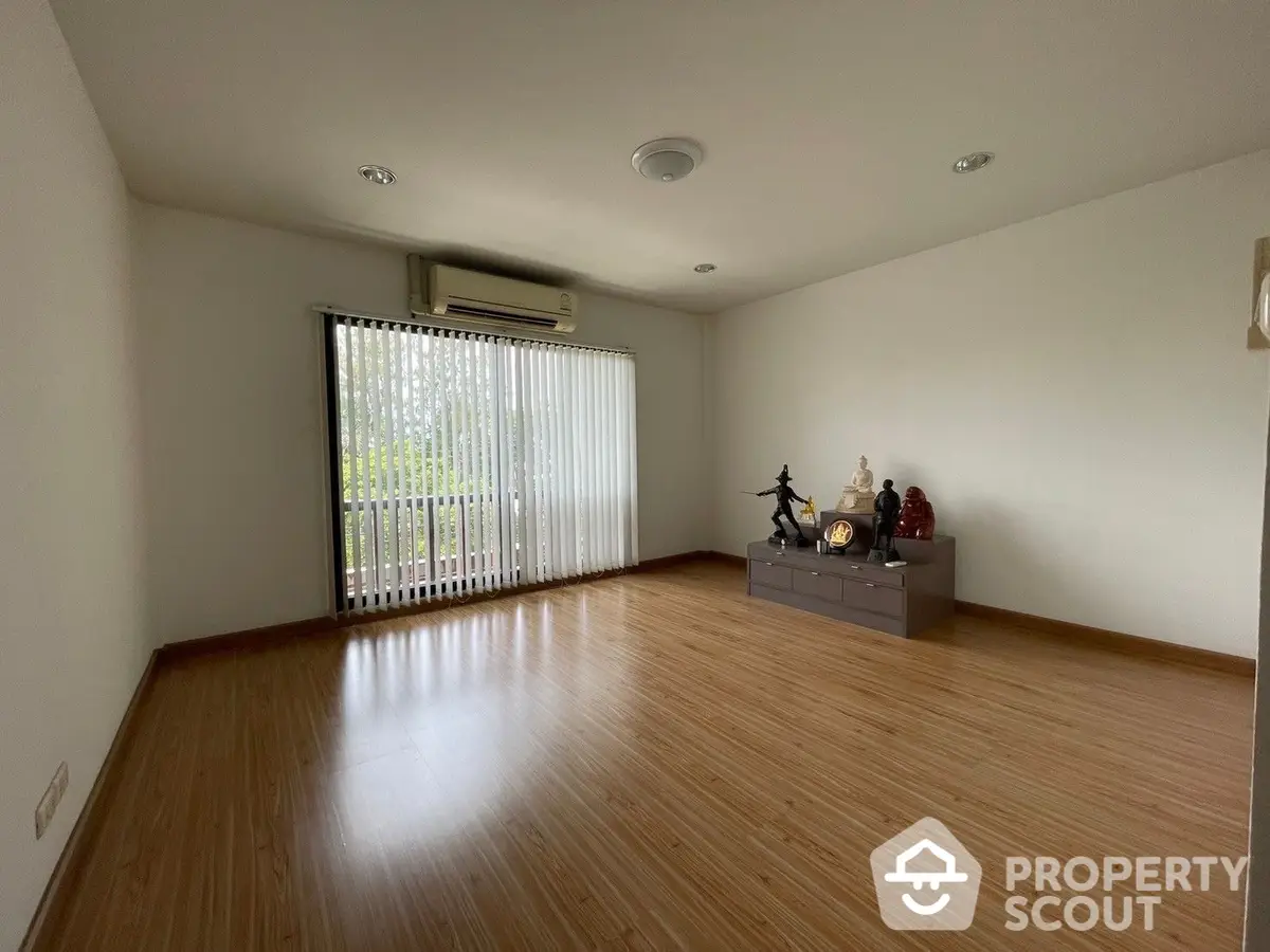 Spacious living room with polished wooden floors and large windows allowing ample natural light, perfect for family gatherings.