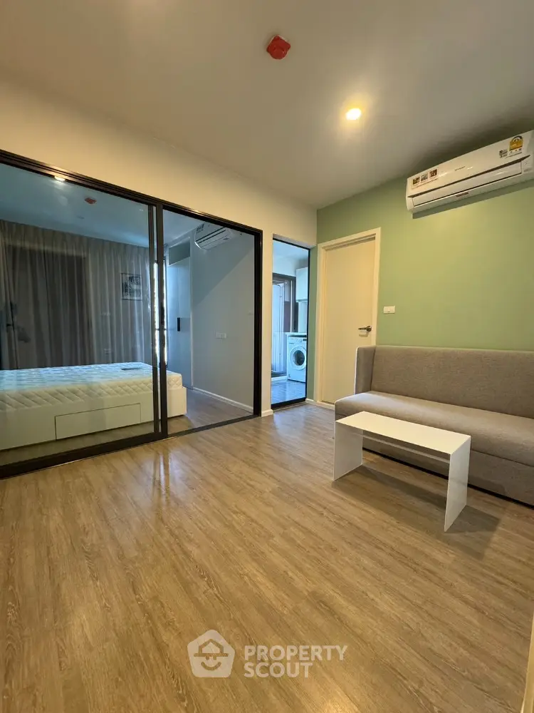 Modern apartment interior with wooden flooring and glass partition, featuring a cozy living area and bedroom.