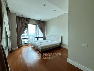Spacious bedroom with large windows and wooden flooring in modern apartment.