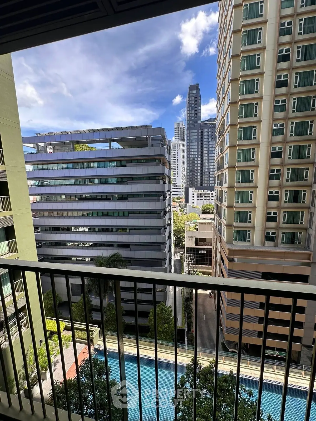 Stunning cityscape view from a high-rise balcony overlooking modern buildings and a pool.
