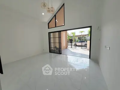 Spacious modern living room with high ceiling and large glass doors opening to a sunny patio.