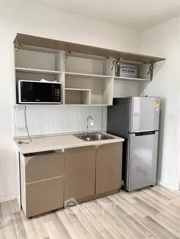 Modern kitchen with sleek cabinetry, microwave, and stainless steel fridge in a compact layout.