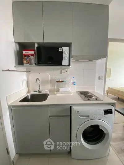 Compact modern kitchen with washing machine and microwave in a stylish apartment.
