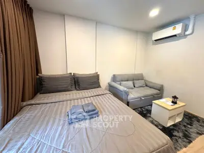 Cozy bedroom with modern decor and air conditioning, featuring a comfortable bed and stylish sofa.