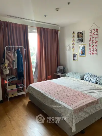 Cozy bedroom with wooden flooring and large window, featuring stylish decor and ample natural light.
