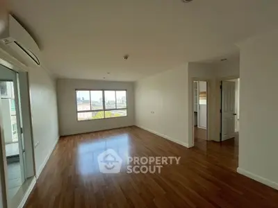 Spacious empty living room with wooden flooring and large window offering city views.
