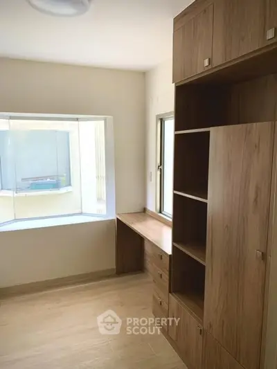Bright study room with built-in wooden shelves and desk, featuring a large window for natural light.